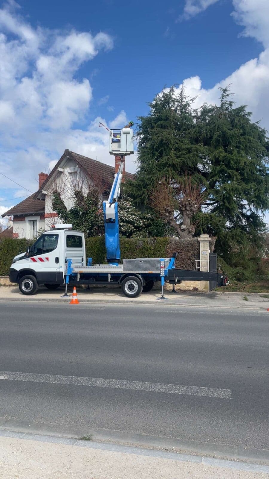 Camion-nacelle stationné au bord d’une route, balisé par un cône de chantier